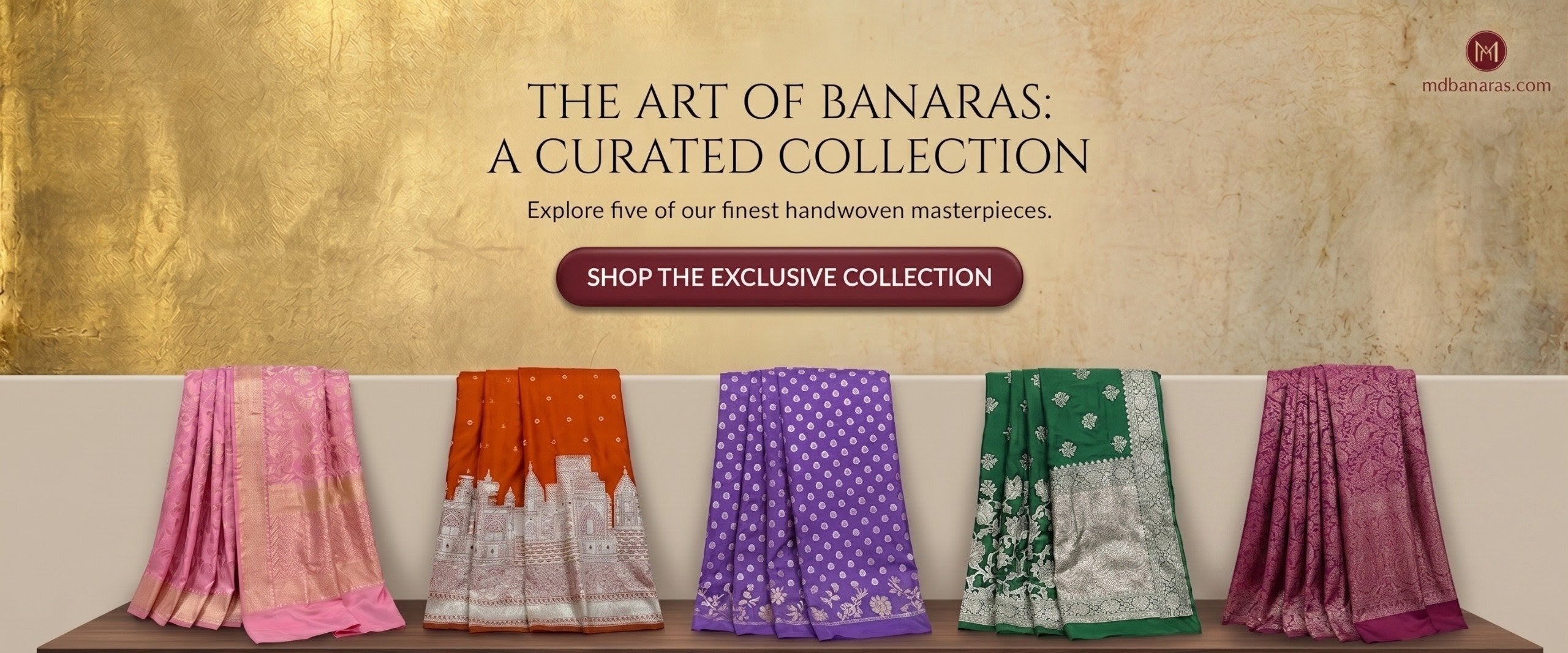 Five handwoven sarees displayed on a wooden shelf with a textured wall background.